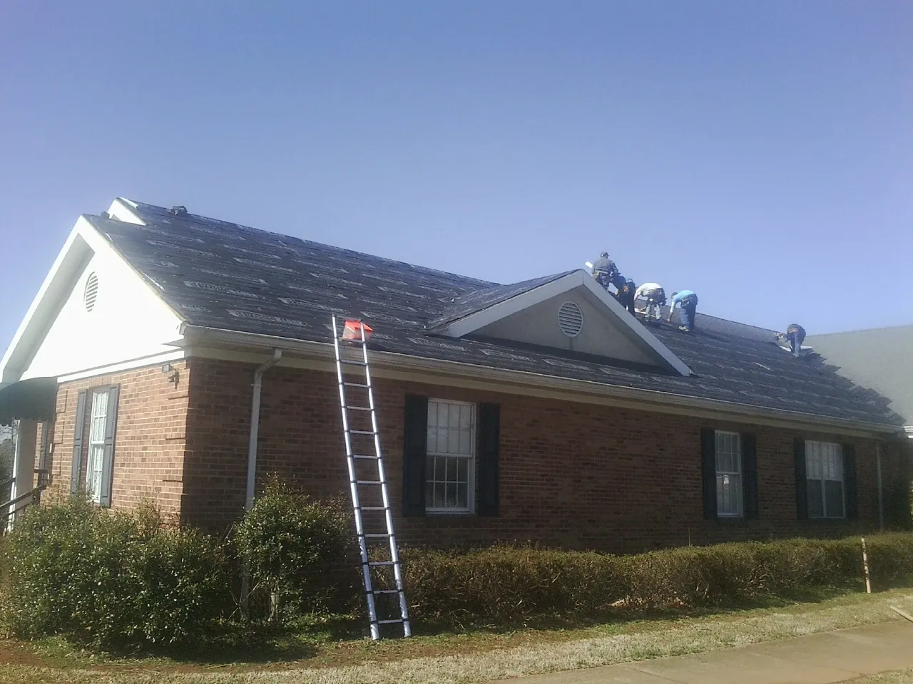 Crew tearing shingles off a brick ranch roof with a ladder set — Emergency Roof Repair work by our crew in Hatfield