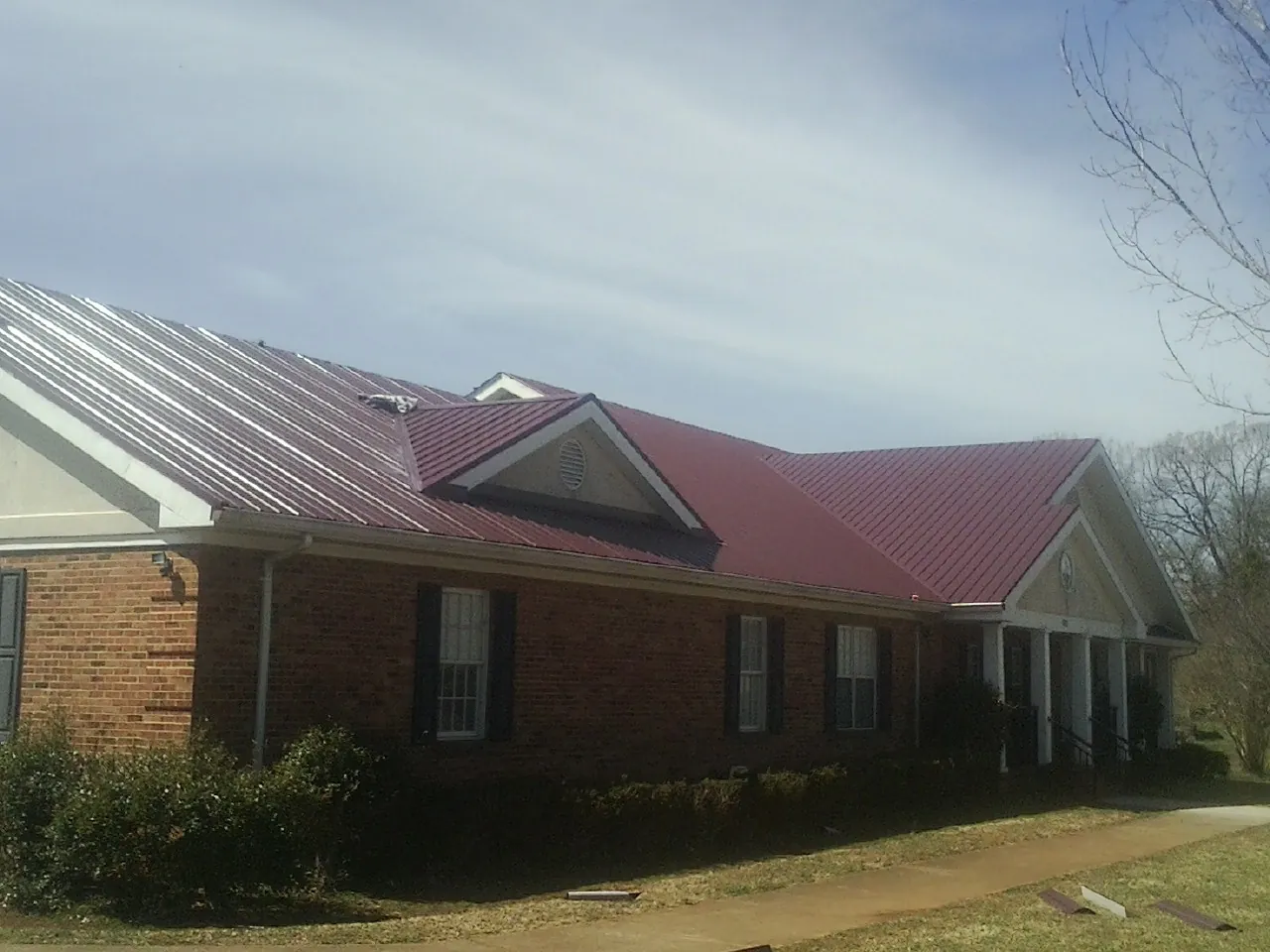 Red metal roof with gabled entries on a long brick building, from a Hail Damage Roof Repair job in Hatfield