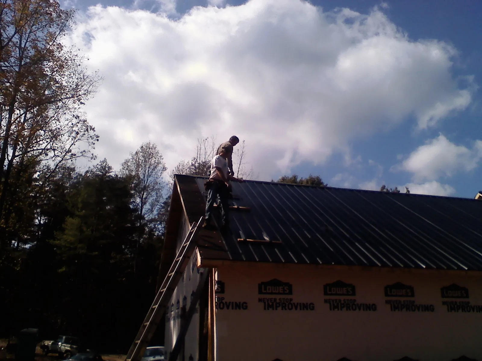 Roofer fastening dark metal panels high against a cloudy sky, from a Roof Inspection job in Hatfield
