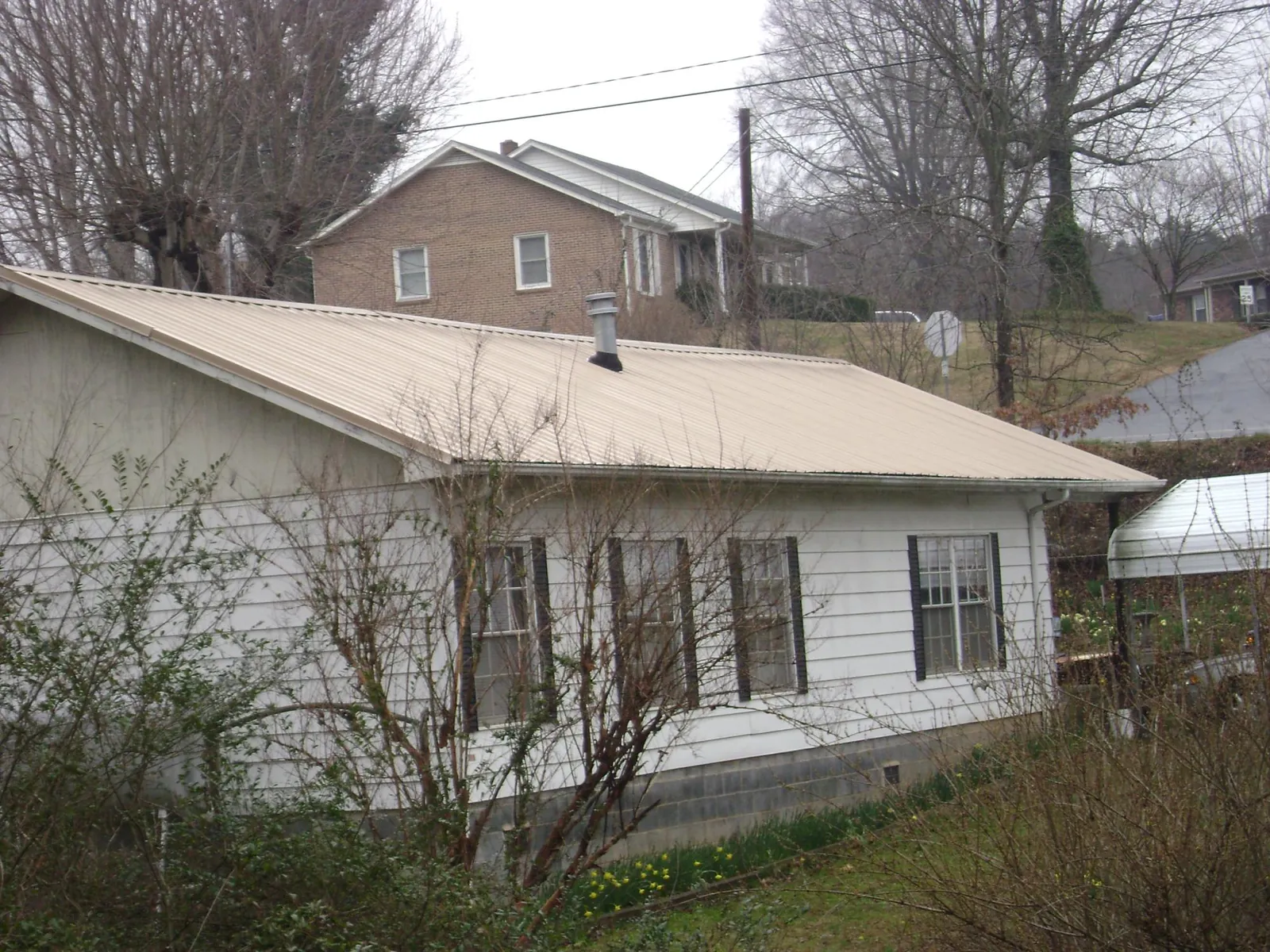 Tan metal roof on a white sided house set into a hillside — Commercial Roofing by Roofing Brothers in Hatfield